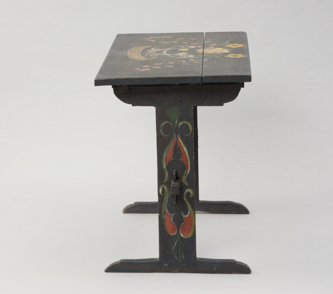 meble - Ujęcie z prawego boku; Stół z malaturą kwiatową na blacie i desce łączącej nogi. Blat prostokątny, wsparty na dwóch wspornikach/nogach w kształcie odwróconej litery 