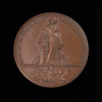medal nagrodowy; nagroda honorowa - Ujęcie awersu. Na awersie stojąca bogini Industria z cęgami w lewej ręce, wspierająca się prawą ręką na młocie, otoczona symbolami rzemiosła i hodowli. W odcinku scena alegoryczna: skrzydlate putto siedzące na orle, po lewej lew, po prawej delfin. Z lewej strony sygnatura. W otoku napis.