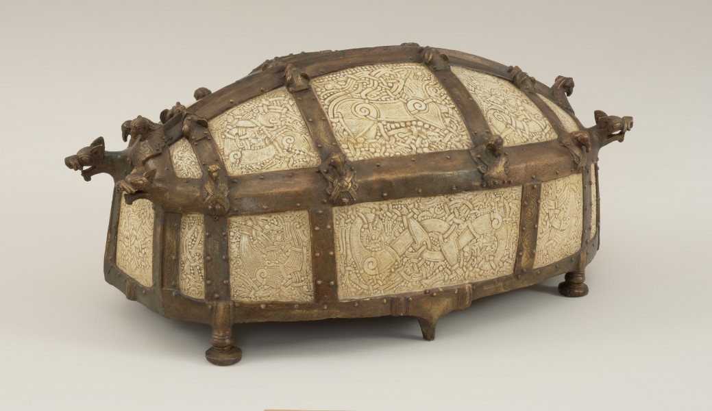 relikwiarz św. Korduli - Ujęcie z tyłu skosem w prawą stronę. Relikwiarz św. Korduli to owalna szkatuła wykonana z 22 płytek z poroża łosia zdobionych w skandynawskim stylu Mammen, którego głównym motywem był element poskręcanych bestii w towarzystwie wątków roślinnych, stosowany od połowy X do połowy XI wieku. Płytki połączono ze sobą za pomocą pozłacanej miedzianej taśmy, której zwieńczenia mają postać smoczych łbów. Dno relikwiarza wykonano z drewna dębowego, a stało ono na sześciu brązowych nóżkach.