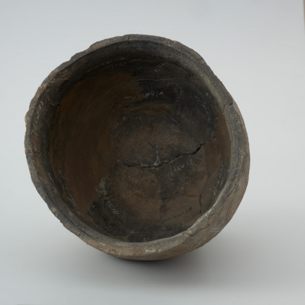 naczynie gliniane - Ujęcie wnętrza. Garnek ma kształt dwustożkowaty o esowatym profilu z charakterystyczną wychyloną na zewnątrz krawędzią wylewu oraz łagodny załom brzuśca znajdujący się w 2/3 wysokości. Na powierzchni pojemnika powyżej załomu występuje zdobienie w postaci krzyżujących się skośnych linii wpasowanych w podwójne, dookolne linie ryte. Naczynie wykonano w technice częściowego obtaczania na kole garncarskim. Uformowano je poprzez sukcesywne klejenie glinianych wałeczków albo taśm. W centralnej części dna znajduje się wklęsły odcisk po ośce, na której obracało się koło. Do produkcji wykorzystano masę garncarską z domieszką schudzającą drobno i średnioziarnistego tłucznia w postaci piasku i granitu.