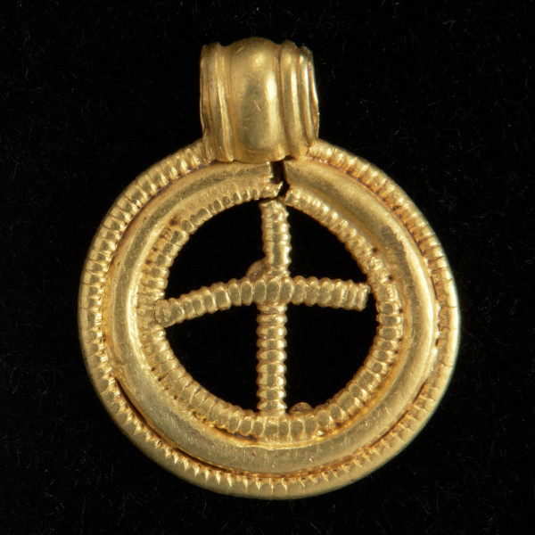 Zawieszka pierścieniowata - Ujęcie z tyłu. Złota zawieszka pierścieniowata wykonana z trzech koncentrycznych pierścieni ze złotego drutu. Pierścień zewnętrzny i wewnętrzny jest pokryty gęstym, perełkowatym karbowaniem. Pierścień środkowy jest niezdobiony. Wnętrze zawieszki wypełnia perełkowaty drucikowaty krzyżyk. Zawieszka posiada uszko ze złotej blaszki.