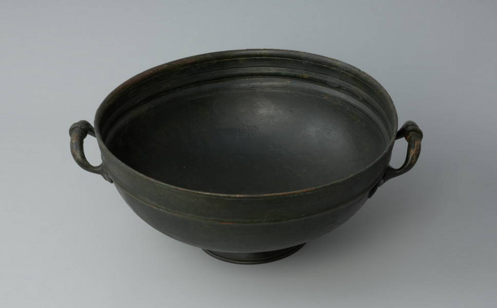 naczynie; Misa z brązu - Ujęcie z góry. Misa z brązu na żebrowanej stopce. Na brzuścu znajduje się nieznacznie wypukły wałek.