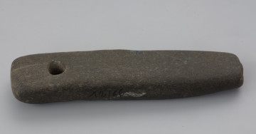 osełka kamienna - Ujęcie z góry. Osełka jest obłego kształt o owalnym zarysie z zaokrąglonymi krawędziami. Na jednym z końców znajduje się otwór przelotowy służący do zawieszania przedmiotu do paska albo na szyi. Na dolnej, górnej oraz bocznej powierzchni można zaobserwować ślady użytkowania podczas ostrzenia.