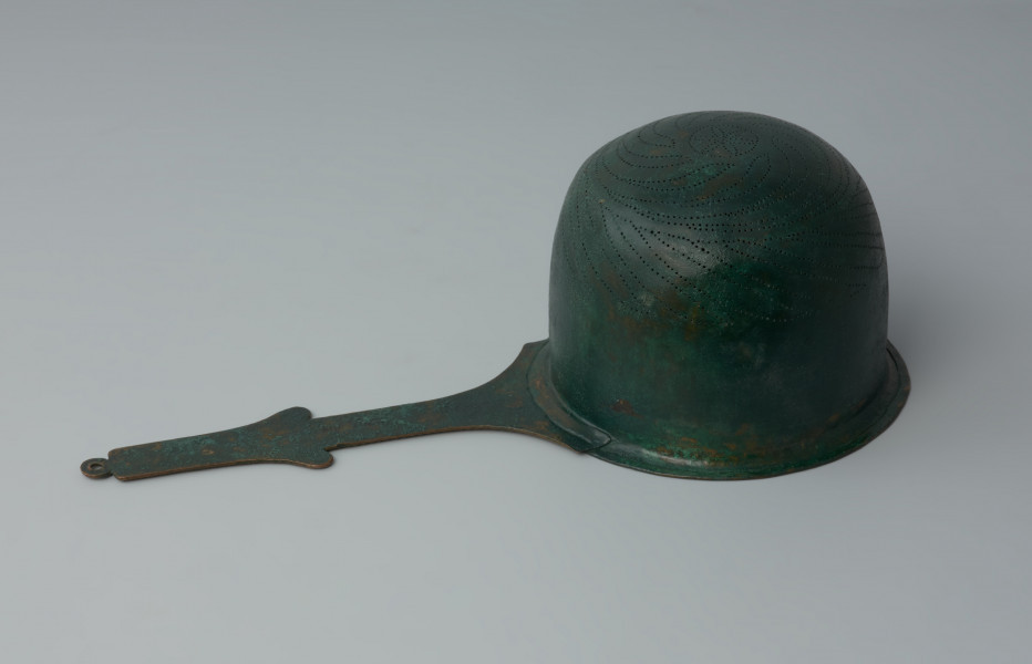 Ujęcie z dołu z lewej strony. Rzymskie cedzidło z brązu z uchwytem zaopatrzonym w woluty.