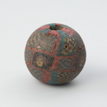 Paciorek szklany z wyobrażeniami kobiecych głów i motywem kobierca - Ujęcie prawego boku. Paciorek szklany z wyobrażeniami kobiecych głów i motywem kobierca. Tło paciorka jest lazurowoniebieskie z rombowymi polami ułożonymi w 4 rzędach.