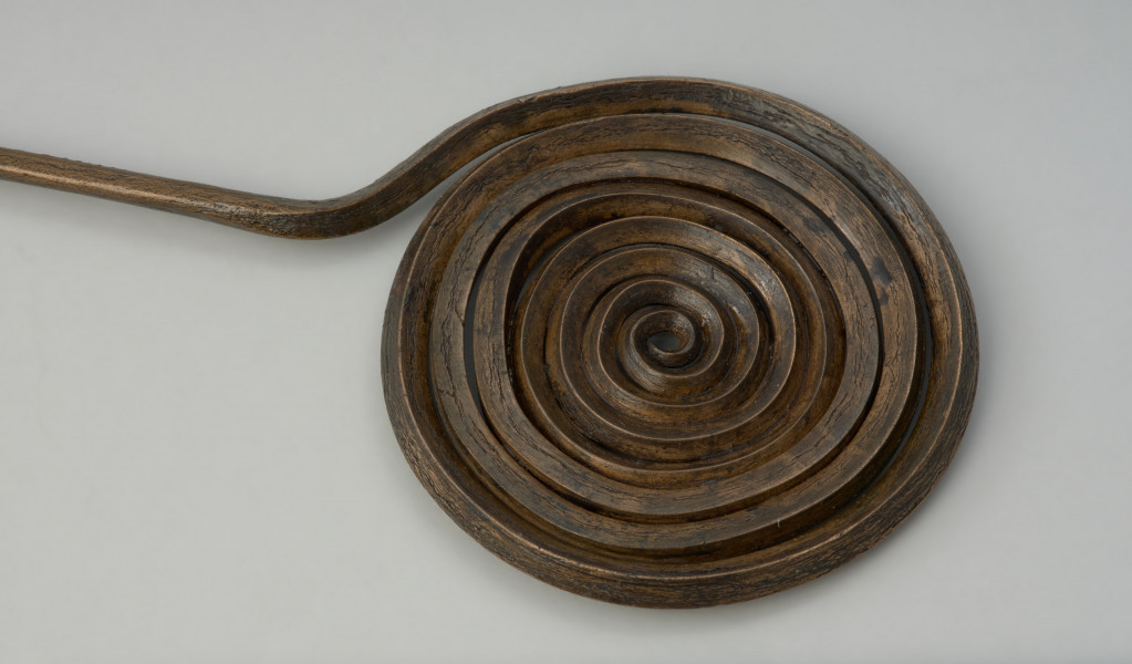 ozdoba stroju; Brązowa szpila - Ujęcie głóki w formie spirali z góry. Brązowa szpila z główkę w formie spiralnej dwunastozwojowej tarczki wykonanej z czworograniastego drutu, natomiast trzpień z okrągłego.