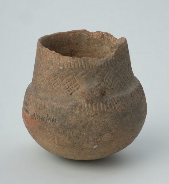 naczynie - ujęcie z boku; Amfora z baniastym brzuścem, prawie cylindryczną szyjką i parą taśmowatych uch umieszczonych niesymetrycznie  u nasady szyjki, zdobiona pod wylewem dookolnymi pasmami pionowych słupków odciskanych, na szyjce stemplami tworzącymi zygzaki i pomiędzy nimi rytymi rombami wypełnionymi ukośną kratką, a na górze brzuśca ponownie dookolnym pasmem pionowych słupków odciskanych