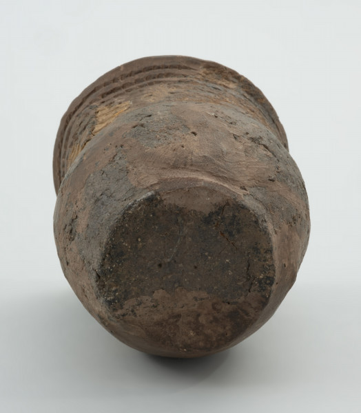 Naczynie gliniane - Ujęcie z dołu dna naczynia;  Puchar o kształcie esowatym, być może pierwotnie zaopatrzony w ucho, zdobiony na szyjce dookolnym pasmem złożonym z 10 rzędów ornamentu odcisków sznura. Naczynie zrekonstruowane na podstawie drobnych fragmentów wylewu, szyjki, brzuśca i dna, uzupełnione barwionym gipsem. Powierzchnia szarobrunatna, z powierzchnią niedokładnie wyrównaną. W masie, na powierzchni widoczna domieszka mineralna.