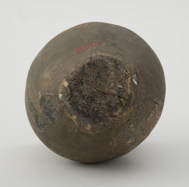 naczynie gliniane - Ujęcie z dołu. Niewielka gliniana waza o kulistym brzuścu i nieznacznie nachylonej do wnętrza szyjce. Wylew wazy jest zaokrąglony. Waza jest zdobiona ponad załomem brzuśca czterema dookolnymi liniami rytymi. Powierzchnia naczynia jest gładka, a barwa ciemnobrunatna. Typologicznie naczynie reprezentuje wazy grupy A grupy dębczyńskiej.