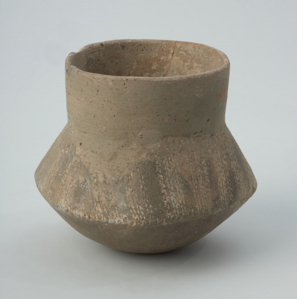 Naczynie gliniane - Ujęcie drugiego boku; Naczynie wazowate o dwustożkowatym brzuścu, pionowej szyjce i niewyodrębnionym dnie. Brzusiec o zarysie czworobocznym w rzucie z góry. Zdobione w górnej części brzuśca ukośnymi pasmami złożonymi z 3 podwójnych linii kreskowo-kłutych wykonanych dwuzębnym narzędziem. Pasma trzykrotnie zmieniają kierunek nachylenia, tworząc układ krokwiasty. Cały układ podkreślony dookolnym pasmem odcisków paznokcia na załomie brzuśca. Szyjka naczynia, niemal w całości zrekonstruowana, prawdopodobnie nie była zdobiona, podobnie jak dół brzuśca