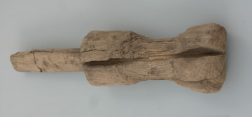 pałka ciesielska - Ujęcie z tyłu. Przedmiot składa się z owalnego trzonka oraz elementu pracującego. Środkowa część zwana potocznie pobijakiem jest mocno wyeksploatowana z obustronnym łukowatym wgłębieniem. Na powierzchni zabytku możemy zaobserwować kilka interesujących śladów powstałych podczas jego produkcji. Są to między innymi podłużne ślady precyzyjnego strugania wykonane za pomocą ostrego noża, jak również lekkie wgłębienia świadczące o użyciu żelaznego ciosła.