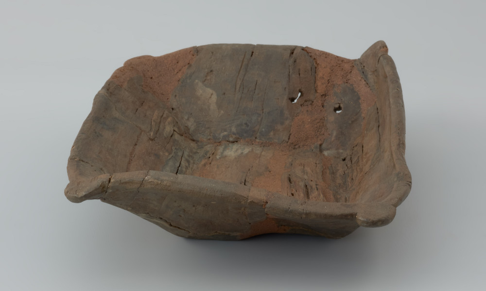 Niecka drewniana; dzieża - Ujęcie prawego krótszego boku lekko z góry. Płytka niecka wydrążona w przepołowionym pniu drzewa liściastego, zaopatrzona w uchwyty ułatwiające przenoszenie