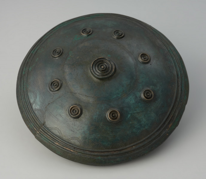 misa do zawieszania - Ujęcie spodu. Misa o dwustożkowatym brzuścu, przechodzącym w niską cylindryczną szyjkę z dwoma prostokątnymi uchami przy krawędzi. Dno naczynia uformowane jest kuliście, jego podstawa zaznaczona jest pojedynczym motywem koncentrycznych okręgów wykonynych w formie plastycznych żeberek. Jest to zarazem punkt centralny całej dekoracji dolnej części naczynia, poniżej załomu brzuśca. Punkt centralny wpisany jest w cztery okręgi. Pierwszy, najmniejszy tworzy wybijany motyw promienisty. Drugi, to podwójne pasmo wybijanych punktów a między nimi pasmo ryte złożone z dwóch linii, połączonych drobnymi ukośnymi nacięciami. Trzeci okrąg składa się ośmiu kolistych koncentrycznych żeberek, analogicznych do żeberek w punkcie centralnym naczynia, ale mniejszych. Ostatni okrąg tworzy potrójne żebrowanie przy krawędzi załomu brzuśca naczynia, połączone z łukowatymi festonami rytymi i wybijanymi. Górną część brzuśca zdobi natomiast linia falista (zygzakowa), także punktowana.