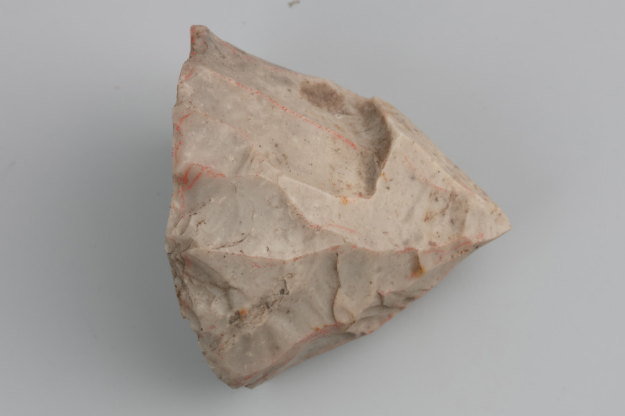 Rdzeń wiórowy jednopiętowy - ujęcie z przodu; Mocno wyeksploatowany rdzeń jednopiętowy podstożkowy wykonany został z krzemienia kredowego dosyć wysokiej jakości. Pięta płaska, bez śladów napraw. Powierzchnia pokryta jest negatywami po krępych i nieregularnych wiórach. Głębokie negatywy sęczków i fal wskazują na wykorzystanie twardego tłuka do produkcji wiórów. Zabytek pokryty jest jasną patyną wskazującą na depozycję w środowisku o lekko kwaśnym odczynie.