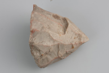 Rdzeń wiórowy jednopiętowy - ujęcie z przodu; Mocno wyeksploatowany rdzeń jednopiętowy podstożkowy wykonany został z krzemienia kredowego dosyć wysokiej jakości. Pięta płaska, bez śladów napraw. Powierzchnia pokryta jest negatywami po krępych i nieregularnych wiórach. Głębokie negatywy sęczków i fal wskazują na wykorzystanie twardego tłuka do produkcji wiórów. Zabytek pokryty jest jasną patyną wskazującą na depozycję w środowisku o lekko kwaśnym odczynie.