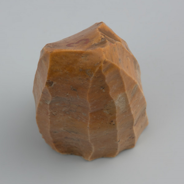 rdzeń wiórowy stożkowaty - ujęcie z góry; Rdzeń stożkowaty o dookolnej odłupni i świeżonej pięcie. Odłupnia ma 12 negatywów po długich, prostych wiórach odbijanych pośrednikiem. Wykonany z krzemienia dobrej jakości. Pokryty jest czerwono-pomarańczową patyną wskazującą na zaleganie w środowisku o dużej zawartości żelaza.