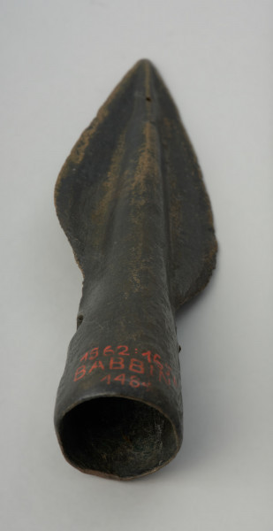 Grot oszczepu - Ujęcie w pionie tyłu grotu. Brązowy grot oszczepu ma smukłą formę oraz wąski liść. Na tulejce znajdują się dwa otwory na nity.