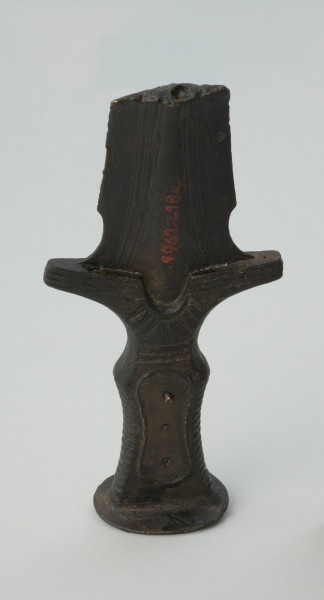 broń, miecz - Ujęcie całej rękojeści z głowicą z tyłu w pionie. Brązowy miecz z czworokatną, dekorowaną żłobieniami rękojeścią, głowicą w formie owalnej tarczki oraz jelcem ze skrzydełkami i półkolistym wycięciem.