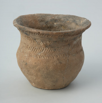 Naczynie gliniane - Ujęcie z przodu; Przysadzisty puchar o szerokim wylewie, zdobiony na szyjce czterema dookolnymi rzędami ukośnych, podłużnych odcisków, które tworzą pasma złożone z dwóch szeregów odcisków układających się w motyw rybich ości. Ukośnymi nacięciami jest zdobiona także krawędź wylewu.