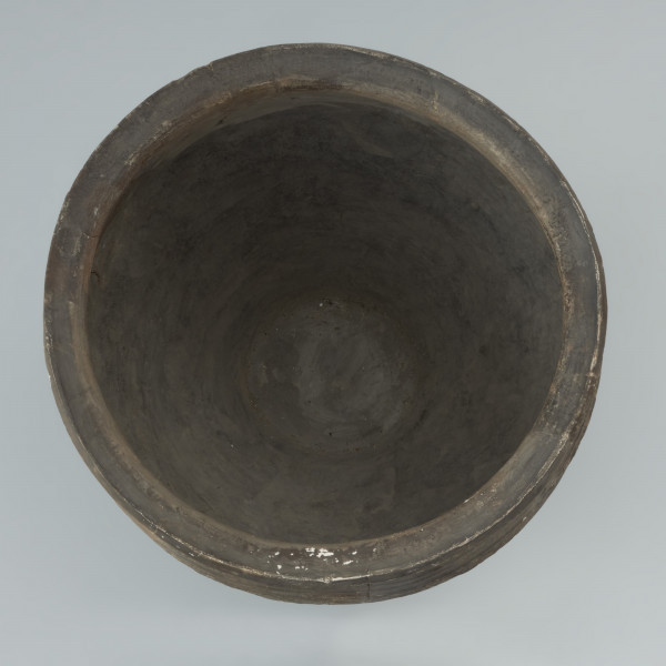 naczynie gliniane - Ujęcie wnętrza nczynia. Garnek o baniastej formie z charakterystycznie wychyloną na zewnątrz krawędzią wylewu, obtoczony w całości na kole garncarskim. Brzusiec garnka znajduje się w 2/3 wysokości. Powierzchnia glinianego pojemnika przyozdobiona jest ornamentem wielowątkowym skośnych żłobków, dookolnych linii rytych, linii falistych oraz ponownych linii rytych. Fakturę naczynia tworzy dobrze wyprofilowana, gładka powierzchnia. Garnek wylepiono z glinianych wałeczków z wcześniej przygotowanej masy garncarskiej zawierającej domieszkę drobno i średnioziarnistego tłucznia - piasku i granitu.