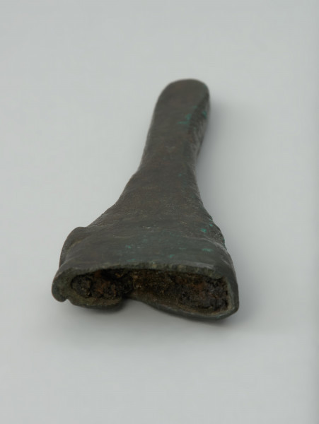 Trzewik pochwy miecza - Ujęcie wnetrza trzewika pochwy miecza. Niezdobiony trzewik pochwy miecza o formie niewielkiego, silnie spłaszczonego lejka, którego powierzchnia jest nierówna i porowata, a krawędź jego nasady uszkodzona.