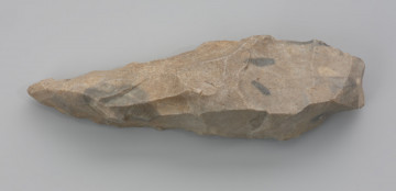 kilof; pik odłupkowy - ujęcie z góry; Pik odłupkowy z Unimia, pow. łobeski. Narzędzie zwane pikiem wykonano z szarego czertu. Jest to skała wieku kredowego, podobna do krzemienia, jednak o bardziej ziarnistej strukturze. Surowiec ten może sprawiać wrażenie trudnego w obróbce, szczególnie w porównaniu ze szklistymi krzemieniami wysokiej jakości. W rzeczywistości jest bardzo łupliwy, uderzony pęka w sposób łatwy do przewidzenia, a jednocześnie jest twardy i wytrzymały. Pik z Unimia został utworzony poprzez odbicie odłupka z dużej bryły surowca. Część pracująca była co najmniej raz naprawiana.