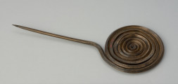 ozdoba stroju; Brązowa szpila - Ujęcie z przodu całej szpili. Brązowa szpila z główkę w formie spiralnej dwunastozwojowej tarczki wykonanej z czworograniastego drutu, natomiast trzpień z okrągłego.