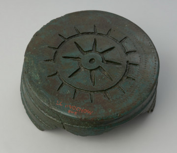 puszka do pasa; Cylindryczna puszka z brązu - Ujęcie spodu puszki z góry. Cylindryczna puszka z brązu z dwoma uszkami na krawędzi. Jest bogato dekorowana na bokach oraz na dnie techniką wybijanych punktów oraz odlewu.