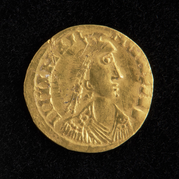 moneta - Ujęcie awersu złotej monety.  Powierzchnie są starte, a treść awersu i rewersu jest częściowo nieczytelna.  Na awersie widnieje schematyczne, zbarbaryzowany wizerunek popiersia cesarza Teodozjusza II przodem, w diademie na głowie i pancerzu na piersi. Po lewej stronie postaci cesarza znajduje się zarys górnego brzegu tarczy.  W otoku znajduje się nieczytelny napis.