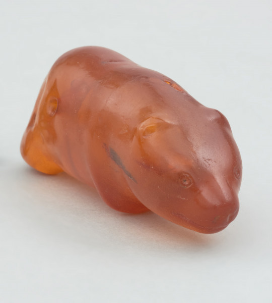 bursztynowa figurka niedźwiedzia ze Słupska - Ujęcie z przodu; Bursztynowa figurka niedźwiedzia. Figurka ma schematycznie przedstawiony tułów i nogi oraz realistycznie oddaną głowę. W momencie znalezienia powierzchnia figurki była matowa i spatynowana, jednak krótko po odkryciu przeprowadzono konserwację zabytku. Także ostro zarysowane oczy, usta i nozdrza są wynikiem prac konserwatorskich. Prawdopodobnie oryginalnie miały bardziej schematyczną formę. Figurka posiada dziurę w tułowiu, która jest efektem formowania się bryłki bursztynu wokół gałązki, która z czasem uległa dekompozycji.