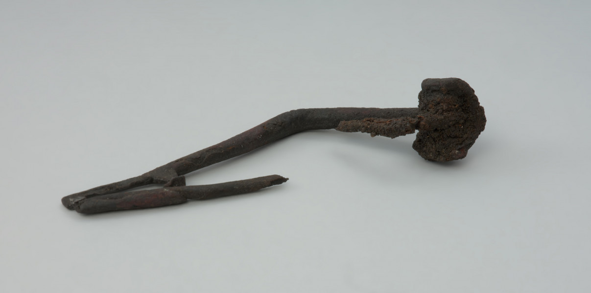 Ujęcie z tyłu. Zapinka żelazna z wybrakowaną szpilą i plastycznym zdobieniem żeberkiem na zgięciu kabłąka.