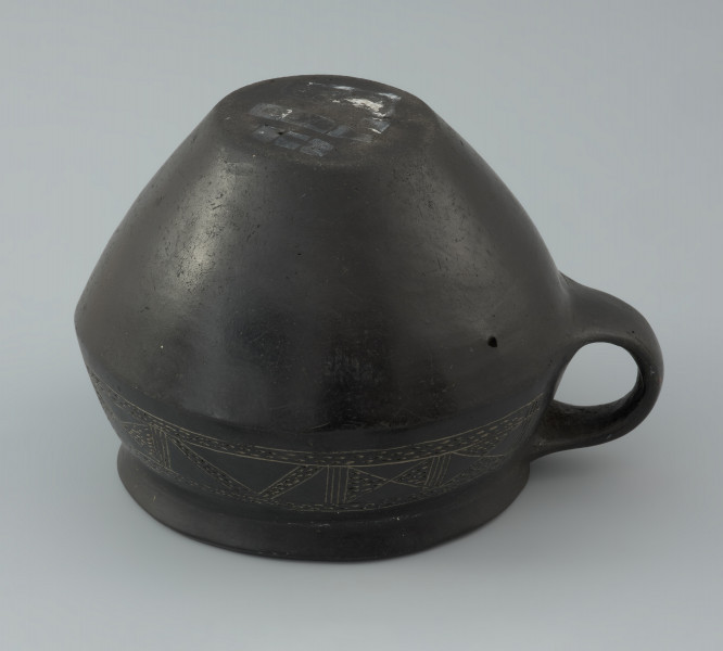 Naczynie gliniane - Ujęcie z dołu. Naczynie gliniane (kubek) posiada gładką, czarną powierzchnię i drobną domieszkę.
