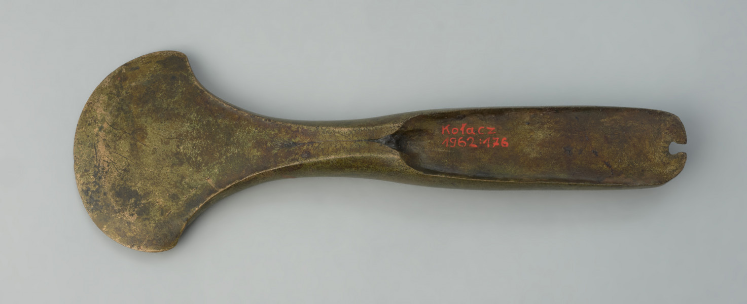 siekierka z piętką - Ujęcie z góry tył.u siekierki. Siekierka brązowa o zabawieniu złocistym z lejkowatą piętką i wąskim, łukowato zakończonym obuchem, na szczycie którego widnieje wyraźna wnęka. Ostrze zostało uformowane wachlarzowato.