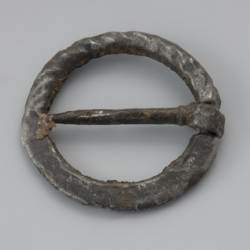Sprzączka żelazna - Ujęcie z przodu z góry w lewą stronę. Sprzączka kolista, żelazna, z płaskim kolcem umieszczonym na wypłaszczeniu ramki. Jedna część ramki jest tordowana