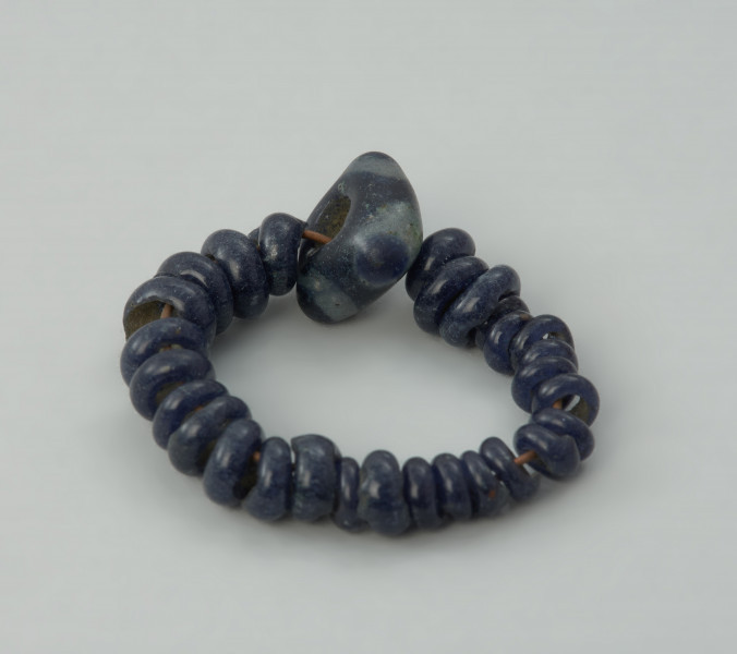 Bransoletka z paciorków szklanych - Ujęcie tyłu bransoletki w poziomie; Zbiór 28 niewielkich paciorków szklanych i jednego większego, najprawdopodobniej tworzących jedną bransoletkę.