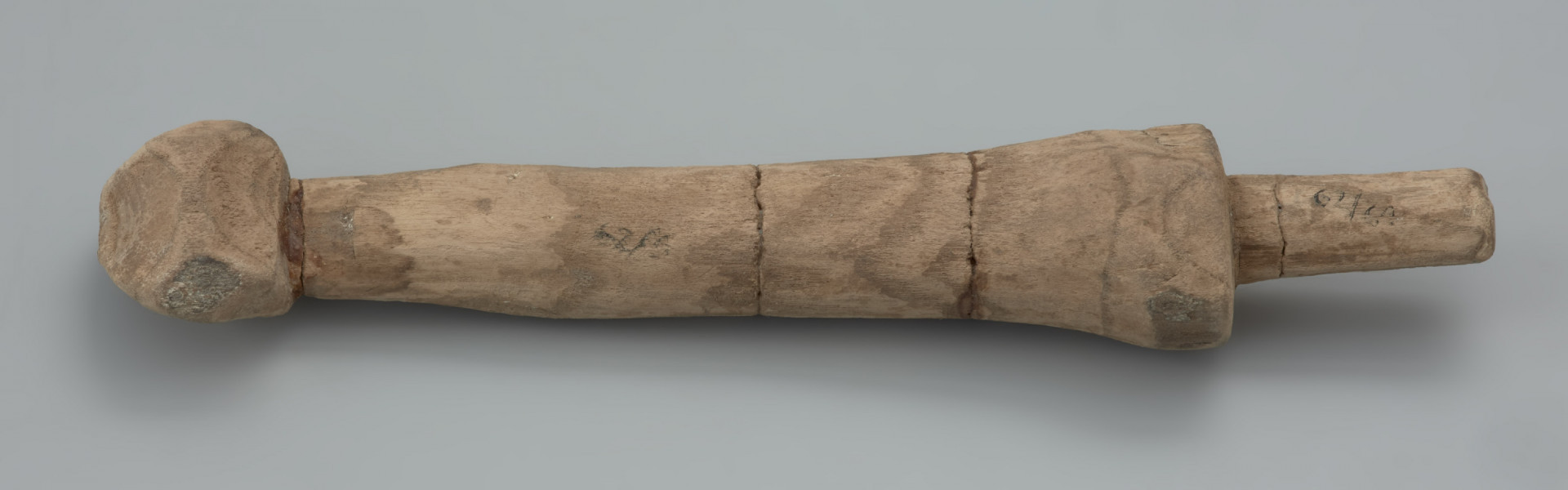 Mieczyk drewniany - Ujęcie z góry przodu skosem w górę.  Drewniany mieczyk-zabawka z okrągłą głowicą kończącą lekko zwężoną rękojeść, bez jelca, z głownią płaską, ułamaną .