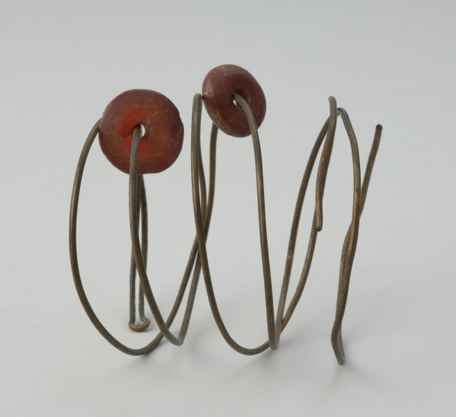 Spirala z brązowego drutu - Ujęcie spirali w poziomie. Trzyzwojowa spirala z cienkiego brązowego drutu, na który nawleczone są dwa bursztynowe paciorki.