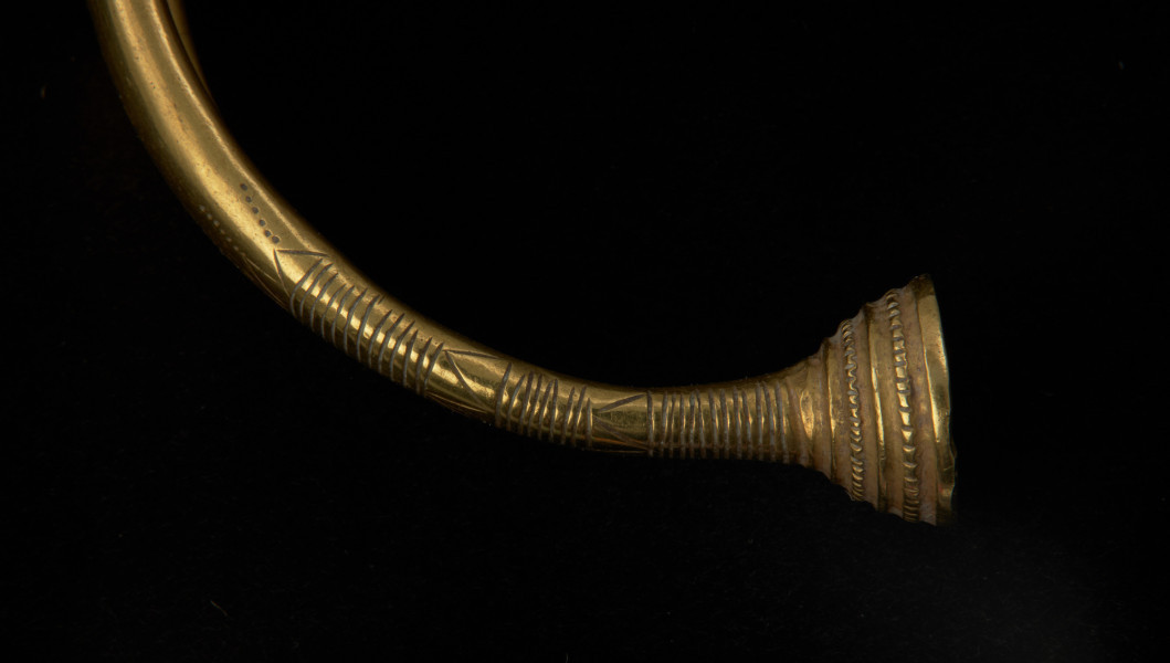 bransoleta z pieczątkowatymi zakończeniami - Ujęcie detalu zapięcia z lewej strony. Bransoleta złota z pieczątkowatymi zakończeniami, którą zdobi żebrowanie, grupy nacięć oraz zygzaki.