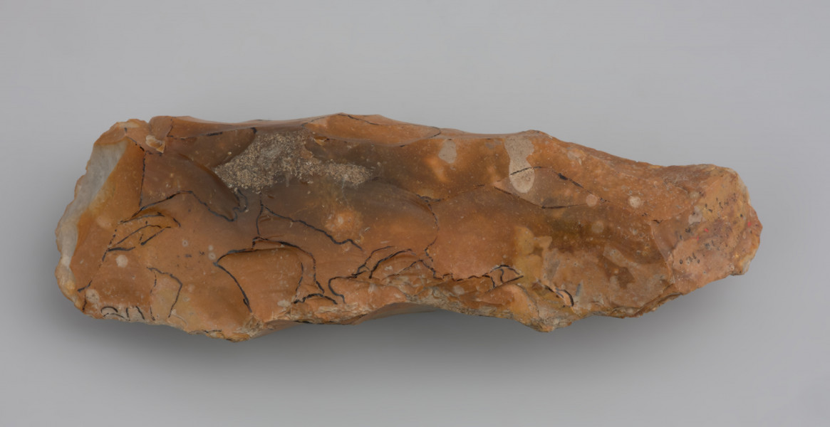 Ciosak rdzeniowy, tzw. typu Lietzow - ujęcie z tyłu; Duży ciosak rdzeniowy, w przekroju romboidalny, tzw. typu Lietzow.  Wykonano go z dużej bryły dobrej jakości krzemienia wydobytej z dna rzeki lub strumienia, o czym świadczy zdarta powierzchnia naturalna i ślady uderzeń o kamienie. Wykonanie narzędzia poprzedziło uformowanie dookolnej krawędzi bryły twardym tłukiem. Następnie odbito kilka serii odłupków w celu jej zmniejszenia i nadania odpowiedniego kształtu. Ostrze uformowano odbiciami po dwóch stronach poprzecznie względem dłuższej osi narzędzia. Ciosak ma liczne ślady uszkodzeń krawędzi, które powstały w trakcie użytkowania oraz napraw ostrza.