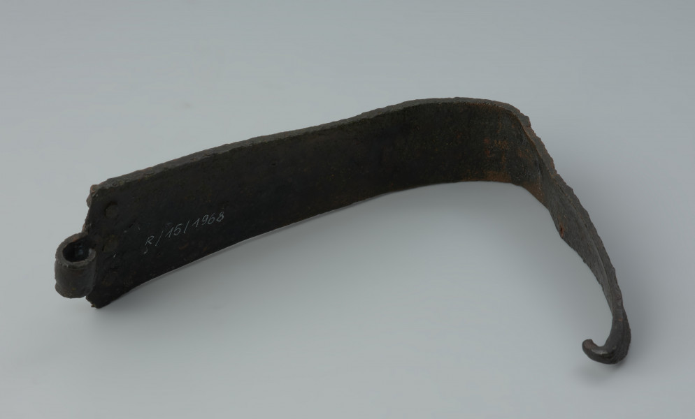 Fragment żelaznej klamry do pasa zdobiony żeberkami - Ujęcie z tyłu. Fragment żelaznej klamry do pasa zdobiony żeberkami. Od strony łącznika znajdują się trzy nity.