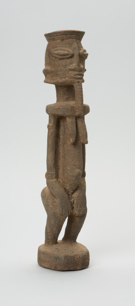 rzeźbiona figura - Ujęcie z przodu, z prawej strony. Drewniana, rzeźbiona postać, z zaznaczonymi jednocześnie cechami płciowymi męskimi i żeńskimi. Wyodrębnione cechy męskie to broda, żeńskie: piersi.