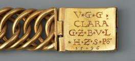 bransoleta z sarkofagu księcia Franciszka I (1577 - 1620) - Ujęcie zapięcia z prawej. Bransoleta wykonana ze skręconych, przenikających się ogniw, w tzw. splocie pancerzowym. Na prostokątnych zapinkach dziewięciopolowy herb Księstwa Pomorskiego trzymany przez dzikich mężów, pierwotnie emaliowany. Na spodzie klamry ryta inskrypcja, pierwotnie emaliowana: V.G.G. / CLARA / G.Z.B.V.L. / H.Z.S.Pō /15.96. Na bocznych ściankach wykonana w tej samej technice inskrypcja: V.G.G. FRANTZ / H.Z.S.Pom.