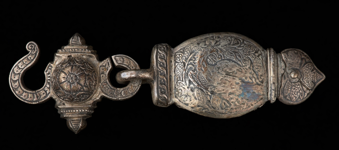 Zapinka pendentu (3części), księcia Kazimierza VI/IX (1557-1605) - Ujęcie prawej części sprzączki. Sprzączka pasa składająca się z trzech elementów. Dwa skrajne o migdałowym kształcie, z jednej strony zakończone profilowanym przewężeniem i łukiem w ośli grzbiet, z drugiej mają przylutowane poprzecznie koliste uszka z gładkiego drutu. Środkowy element sprzączki,zdobiony jest guzem ujętym od góry i dołu profilowanymi sterczynami; po prawej stronie uszko, którym połączony jest z bocznym elementem zapinki, a po lewej - esowato wygięty haczyk, służący do zapinania pasa. Wszystkie części zapinki pokryte są gęsto grawerowaną, niellowaną dekoracją z motywami ptaków wśród wici roślinnej oraz stylizowanych kwiatów i ornamentem geometrycznym.