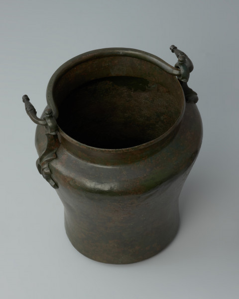 Ujęcie z góry. Situla (wiadro) z brązu z tzw. ataszami w postaci stylizowanych postaci delfinów.