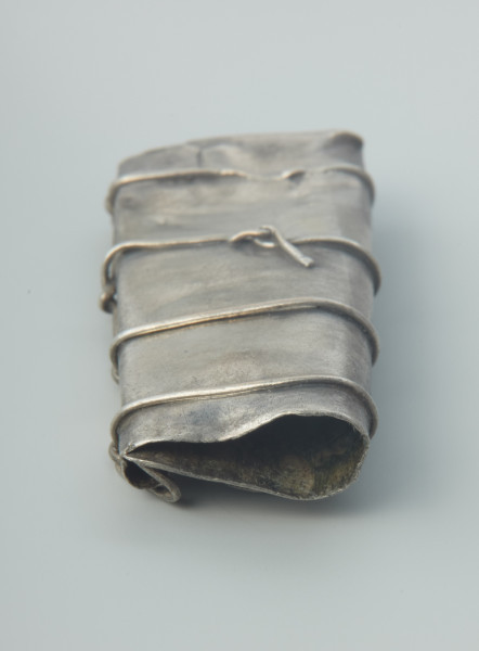 Kaptorga - Ujęcie w pionie prawej strony kaptorgi.  Kaptorga, prostokątna zawieszka ukształtowana ze srebrnej blachy zagiętej wpół, zawiniętej z jednej strony w długie, rurkowate uszko, pod którym jest przylutowany drugi koniec blachy. Jeden bok jest zamknięty poprzez zagięcie na siebie bocznych krawędzi blachy, drugi natomiast pozostawiono otwarty. Do przedniej ścianki kaptorgi przymocowane zostały cztery prostokątne, pionowo ułożone, blaszki z wytłoczonymi guzkami. Całość oplata drucik przechodzący przez każdy guzek i biegnący wzdłuż rurkowatego uszka. Przedmiot został odkryty w 1933 roku w Dobrociechach w nieznanych okolicznościach i pochodzi ze skarbu monet i ozdób srebrnych