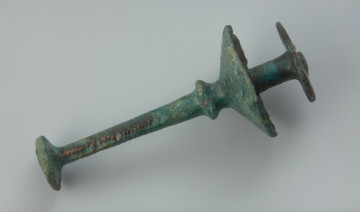 Brązowy tutullus z dwiema tarczkami. - Ujęcie w poziomie z boku skosem do przodu. Brązowy tutullus, który posiada zdobienie na większej tarczce oraz trzpieniu w postaci linii oraz ukośnych kreskach.