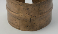 bransoleta taśmowata - Ujęcie przodu bransolety. Bransoleta otwarta wykonana z wąskiej, dość grubej taśmy brązowej o przekroju płasko-wypukłym. Końce obręczy są ścięte prosto, a jej powierzchnię pokrywa ornament ryty złożony z grup ukośnych i pionowych kresek, poprzedzielanych motywem jodełki.