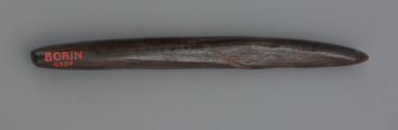 grot; ostrze kościane - ujęcie tyłu; Krótkie ostrze kościane o owalnym przekroju, wykonane z kości długiej dużego ssaka. W części środkowej po dwóch stronach widoczna jest płaska, naturalna powierzchnia kości. Na powierzchni widoczne są liczne, podłużne linie ryte i poprzeczne prążkowanie, świadczące o intensywnym użytkowaniu i wielokrotnych naprawach. Pierwotnie ostrze mogło być dłuższe, zaś z każdą kolejną naprawą ulegało skróceniu. Na skutek przebywania w torfowisku powierzchnia zabytku trwale przybrała ciemny, niemal czarny kolor.