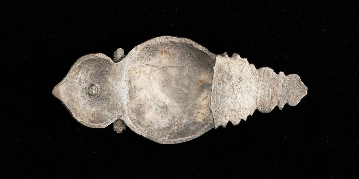 okucie końca pendentu księcia Kazimierza VI/IX (1557-1605) - Ujęcie z tyłu. Okucie końca pendentu o migdałowym kształcie, u góry w przewężeniu profilowana przepaska, nad nią zwieńczenie w kształcie łuku w ośli grzbiet. Dolna część profilowana, o trójkątnym zarysie. Okucie w całości pokryte grawerowaną, niellowaną dekoracją z motywem ptaka wśród wici roślinnej, stylizowanych kwiatów i ornamentów ciągłych. W górnej części, pośrodku łuku w ośli grzbiet - okrągły otwór z nitem.