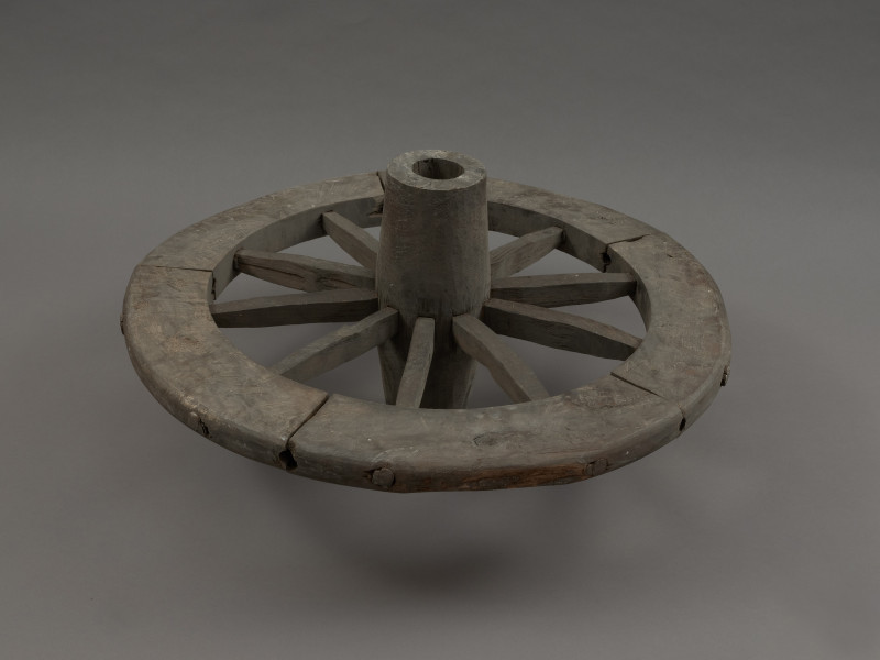 koło - Ujęcie z boku. Replikę koła szprychowego wykonano na podstawie znalezisk z badań wykopaliskowych na Starym Mieście w Kamieniu Pomorskim. Jest produktem kołodzieja, inaczej stelmacha, rzemieślnika zajmującego się wyrobem wozów drewnianych. Poszczególne elementy koła zrobione są z różnych gatunków drewna.